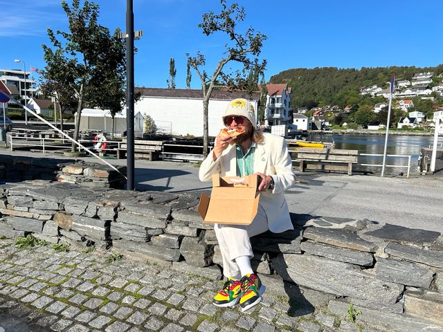 Tom Egill spiser pizza i Vikevåg etter Rennesøydagen, med bøttehatt på hodet.